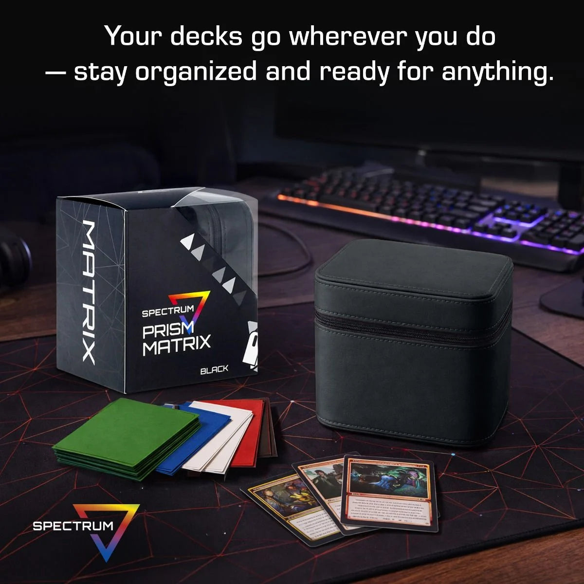 BCW Prism Deck Case - Matrix in black, featuring card dividers and sleeved cards, with a gaming desk setup in the background.
