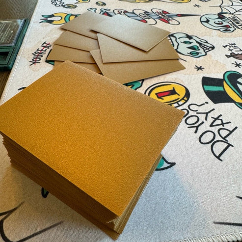Nerd Gear Rock Guard Premium MTG Textured Matte Sleeves - 110 Pack shown in a stack on a playful tablecloth, highlighting their glittery gold appearance.